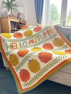 a crocheted blanket with apples and pumpkins on it sitting on a couch