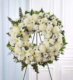 a wreath with white flowers and greenery is displayed on a stand in front of a door