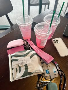 three plastic cups sitting on top of a table next to a cell phone and purse