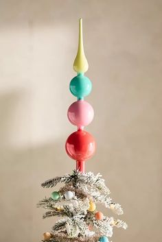 a small white christmas tree with colorful ornaments on it's branches and balls hanging from the top