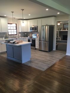 a kitchen with white cabinets and stainless steel appliances, hardwood floors, and an island in the middle