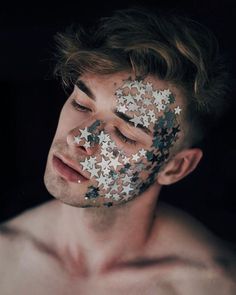 a shirtless man with his face covered in silver and black stars, looking at the camera