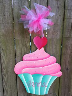 a cupcake with pink frosting and a heart on top hanging from a wooden fence