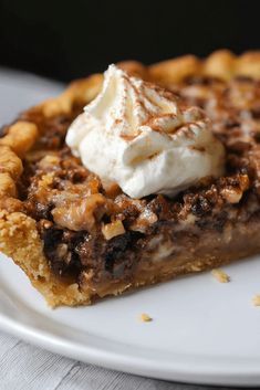 a slice of pecan pie with whipped cream on top sits on a white plate