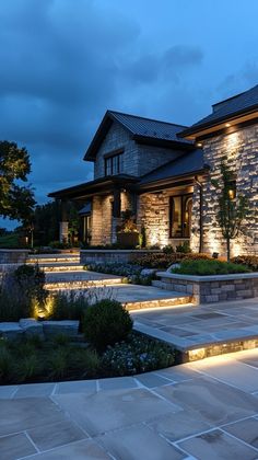 a house that is lit up at night with lights on the steps and landscaping around it