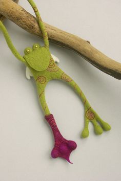 a stuffed frog hanging from a branch on a white surface with pink and green accents