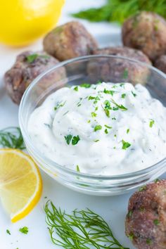 a small bowl filled with white sauce next to some meatballs and lemon wedges