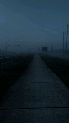 an empty road in the middle of a foggy night with traffic lights and street signs