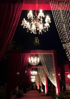 an outdoor wedding venue decorated with red drapes, chandeliers and white lights