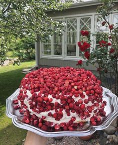 someone holding up a cake with strawberries on it in front of a house and flowers