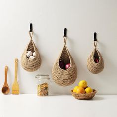 three crocheted baskets hanging on the wall with spoons and lemons next to them