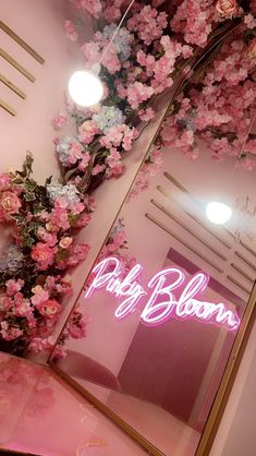 pink flowers are growing up the side of a wall in front of a neon sign