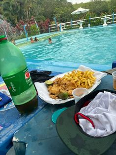 a table with plates of food next to a pool filled with people swimming in the water