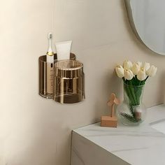 a vase with white flowers sitting on top of a counter next to a mirror and toothbrush holder