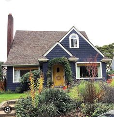 a blue house with yellow door surrounded by greenery and flowers on the front lawn