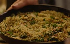 a pan filled with rice and vegetables being held by a person's hand in the background