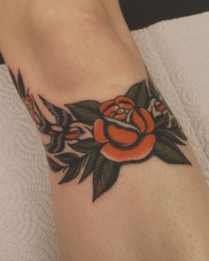 a rose and two birds tattoo on the left side of the leg, with leaves around it