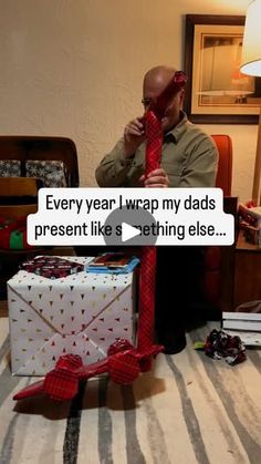 a man sitting on the floor with a red tie around his neck and an envelope in front of him that says, every year i wrap my dads present like something else