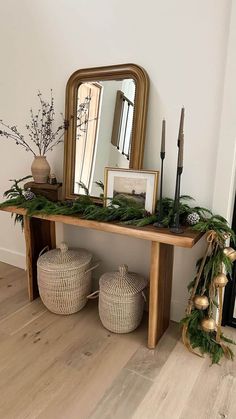 a wooden table topped with lots of greenery next to a mirror and two wicker baskets