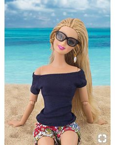 a doll sitting in the sand with sunglasses on her head and long blonde hair wearing shorts