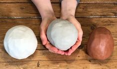 two hands holding three different types of rocks on a wooden surface, one is white and the other is brown