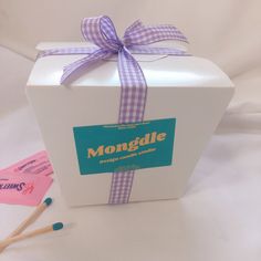 a white box with a purple ribbon on it and two matchsticks next to it