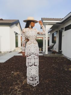 a woman wearing a white dress and hat standing in front of a house with her hand on her hip