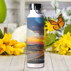 a water bottle sitting on top of a wooden table next to flowers and a butterfly