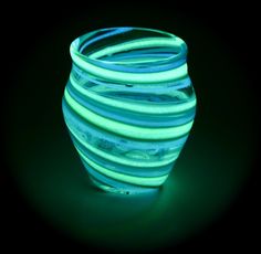 a green and blue striped vase sitting on top of a table next to a black wall