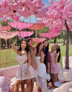 four women standing under pink umbrellas in front of a tree with flowers on it