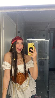 a woman dressed as a pirate taking a selfie with her cell phone in the mirror