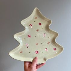 a hand holding up a white ceramic christmas tree dish with candy canes on it