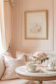 a white table with two cups and saucers on it in front of a window