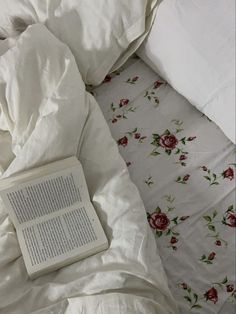 an open book sitting on top of a bed next to pillows and blankets with roses