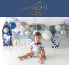 a baby boy sitting on the floor in front of balloons and garlands for his first birthday