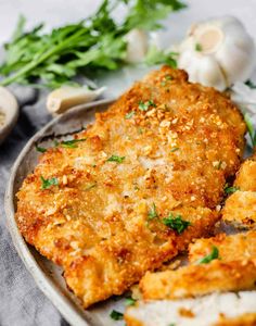 two pieces of fried chicken on a plate with garlic and parsley next to it