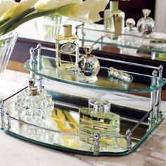 two glass shelves with perfume bottles and flowers in them on a marble countertop next to a mirror