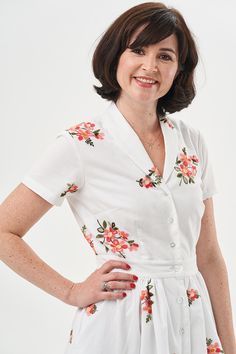 a woman wearing a white dress with pink flowers on it and smiling at the camera