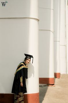 a woman in a graduation gown leaning against a column