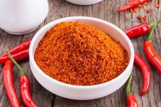 red chilli powder in a white bowl surrounded by chili peppers on a wooden table