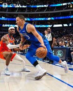 two basketball players in blue and orange uniforms are on the court with an audience watching