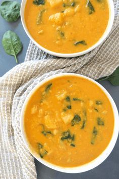 two bowls of soup with spinach and cheese on the top, next to one another