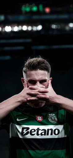 a soccer player covers his face with his hands as he stands in front of the camera