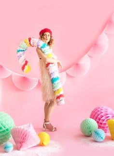 a woman standing in front of pink backdrop with paper balls and tissue pom poms