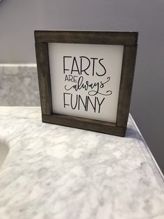 a framed sign that says farts are always funny on the counter in a bathroom