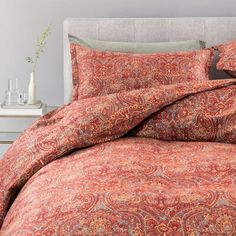 an orange and red bed with paisley print on the comforter, pillows and pillow cases