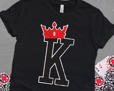 a black t - shirt with the letter k and a crown on it, surrounded by poker chips