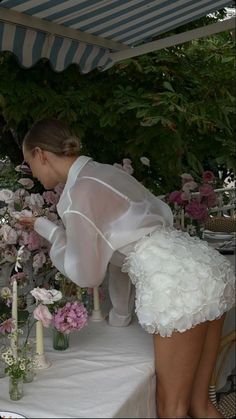 a woman in white dress standing over a table with flowers