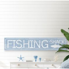 a fishing shack sign hanging from the side of a wall next to a plant