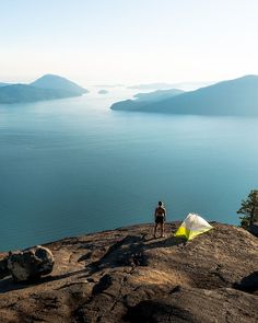 a man standing on top of a mountain next to a tent